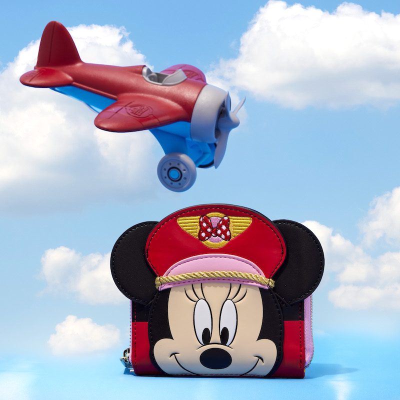 Red and pink wallet with an appliqué of Minnie Mouse on the front dressed as a pilot with a red and pink hat. The wallet sits against a background that looks like the sky with a red and blue airplane flying above.